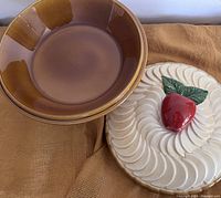 Photo of the ceramic pie plate and its lid placed on a cloth, showing the brown plate and the cream lid with a red apple handle.