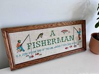 Front view of vintage fishing embroidery art framed in wood, showing colorful fishermen and fish designs with text.