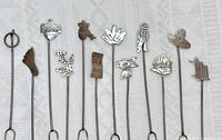 Full set of 12 sterling silver Mexican cheese picks arranged horizontally on fabric background, showing all unique charms.