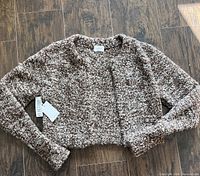 Full view of a brown and beige cropped cardigan laid flat on wood floor showing the texture and fit, new with tags attached.