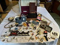 Overview of the lot spread on table showing all items including cast iron decor, jewelry, pins, leather notebook, cases, and various small collectibles.