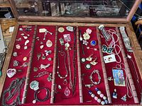 Top view of wooden case showing overall red velvet lining and multiple compartments filled with assorted jewelry and collectibles.