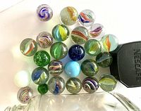 Overhead view of the 25 marbles showing various colors and swirl patterns along with a Nescafe coffee jar lid for size comparison