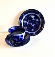 Handleless cup on deep saucer with matched flow blue small plate in background showing dark rich blue pattern.