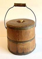 Front view of antique wooden firkin showing wood staves, metal strapping, wooden lid, wire handle with wooden grip