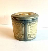 Front view of the antique salt glaze covered crock showing decorative embossed panels and lid.
