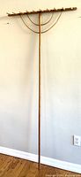 Full view of the antique wooden rake hanging against a wall showing the long straight handle and wide rake head with nine prongs.