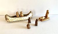 Photo of carved wooden vignette with man, duck on sled, three small signed figures, and birchbark canoe with two figures