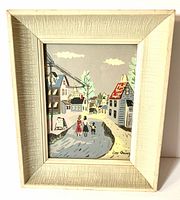 Front view of vintage framed picture signed Geo Quincy depicting a village street scene with three people under a cloudy sky in muted colors.
