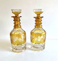 Front view of two amber and clear glass decanters featuring frosted grape and vine designs with matching stoppers.