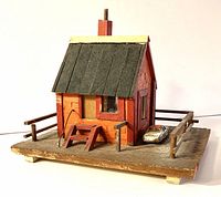 Three quarter view of the vintage hand-crafted wooden house diorama on a wooden base with railing and a small toy car parked beside the house.