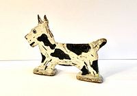 Side view of vintage cast iron terrier dog boot scraper painted white with black spots showing the length and height proportions.