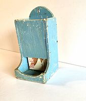 Side angled view of vintage wooden match holder showing paint wear, chips, and partially used Redbird matchbox inside