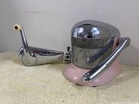 Side view of pink Juice-O-Mat with shiny chrome top and chrome lever arm alongside the white Can-O-Mat can opener with chrome arm and cream handle knob, placed on a yellow towel.