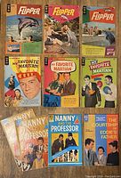 Top view of all 10 comic books arranged in rows on a wooden surface, showing full covers and titles of each comic from the 1960s TV shows.