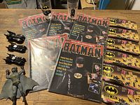 Photo of five Batman movie magazines, three Batmobile models, two Batman glass cups, and six Batman cup ads laid out on a table