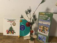 Photo of original box of musical Charlie Brown Christmas tree with tree and green vinyl LP record in front of it