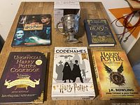 Top-down view of all five Harry Potter related books and the boxed silver mug placed on a wooden surface.
