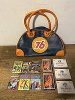 Vintage 76 gas station bag in blue and orange vinyl with handles, and set of six small comics displayed in front of the bag.