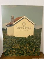 Front view of Veuve Clicquot promotional poster showing vineyard scene with branded building.