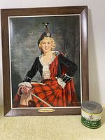 Frontal photo of the framed portrait and Export A tin together on floor