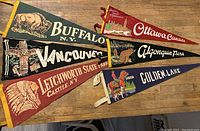 Set of six vintage felt pennants displayed together, showing colorful artwork and text for Buffalo N.Y., Vancouver, Letchworth State Park, Ottawa, Algonquin Park, and Golden Lake locations.