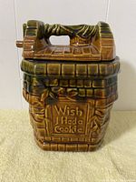 Front view showing inscription and design of the cookie jar resembling a wishing well, color hues and visible condition.