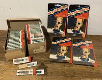 Lot overview showing two open boxes of Wrigley's Snappy Gum packages stacked together and four individually packaged Max Headroom air fresheners laid out to the right, all resting on a wood surface.
