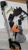 Full view of all items including the electric lawn mower handle, pruning shears, gloves, battery packs, charger, saw blade, and guard.