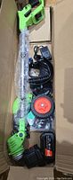 Packed green and black lawn mower with battery, charger, cutting blades, guard, and handles in box