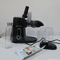 Full view of AMZCHEF juicer machine with clear juice container, feeding chute attached, power cord with control knob, and user manual.