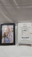 Photo showing the front of the sealed black rectangular photo frame and the back of the package of 25 thank you cards with envelopes.