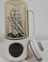 Full view of soy milk maker with transparent jar, handle, power cord inside jar, base and detached lid