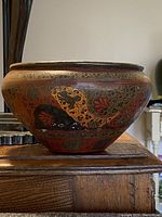 Side view of rounded brass bowl showcasing engraved and painted cloisonné floral and paisley patterns in black, red, and gold.