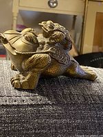 Side and angled side views showing the brass money frog with detailed coin patterns on its back and carved features.