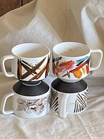 Four Starbucks ceramic mugs displayed with unique abstract designs and black bottoms, shown with handles oriented differently to highlight artwork.