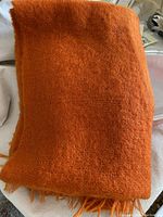 Folded vintage coral-colored mohair and wool couch throw, showing woven texture and fringes at the edges.