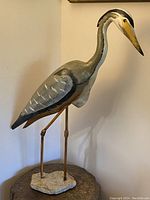 Full view of the wooden life-size carving of a Great Blue Heron mounted on stone base.
