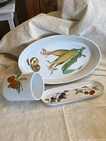 Full view of three porcelain pieces: oval platter, cylindrical container, and small elongated tray with fruit designs