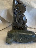 Two dark soapstone Inuit figurines on beige fabric background; human figure and seal; human figure has carved facial features and wears a necklace