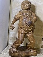 Front view of the wood carving showing the man with closed eyes, holding a glass in one hand and stepping forward, detailed carving of clothing and facial features.