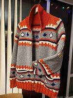 Front view of sweater hanging, showing zip closure, shawl collar, fair isle pattern and two front pockets