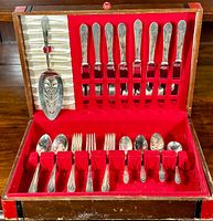 Full set of WM Rogers Manhatten pattern triple silverplate flatware displayed in a wooden chest lined with red velvet and cream satin backing, showing all included items securely held.