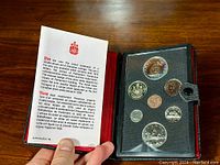 Open black leather case with red satin interior showing seven Canadian coins and a descriptive insert.