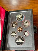 Front view of the seven 1983 Canadian coins displayed in a plastic holder inside a black leather case with red interior.
