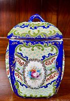 Front view of square porcelain lidded jar with cobalt blue background and floral hand-painted medallion on panel