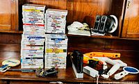 Two tall stacks of Wii game cases flanked by remotes and accessories on wooden surface