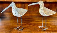 Two carved wooden shore bird sculptures with metal legs, displayed on wooden surface