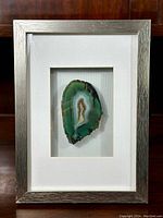 Front view of the framed agate slice showing the silver frame and white matte around the green agate slice.