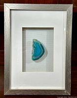 Framed green agate slice with silver frame and white matting, displayed upright on a wood surface.